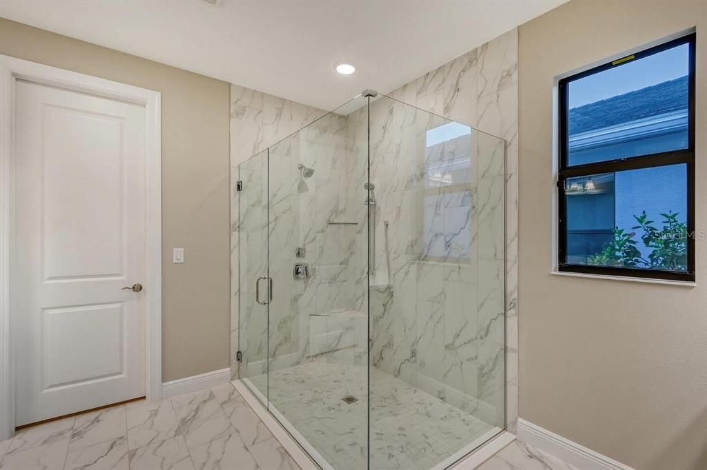 The luxurious owners ensuite bathroom with quartz countertops, his and her vanities, a frameless glass-enclosed walk-in shower including a Moen handheld shower w’side bar, and a spacious walk-in closet.