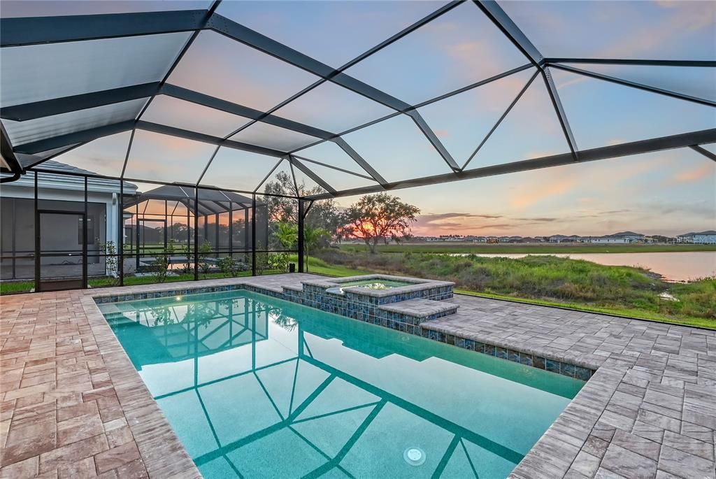 The extended screened-in covered lanai, complete with an extended-30ft heated Pebble Tec saltwater pool and spa with water features, an outdoor kitchen hookup, picture frame screening, and rare preserve and lake view!