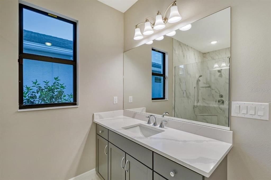 The luxurious owners ensuite bathroom with quartz countertops, his and her vanities, a frameless glass-enclosed walk-in shower including a Moen handheld shower w’side bar, and a spacious walk-in closet.