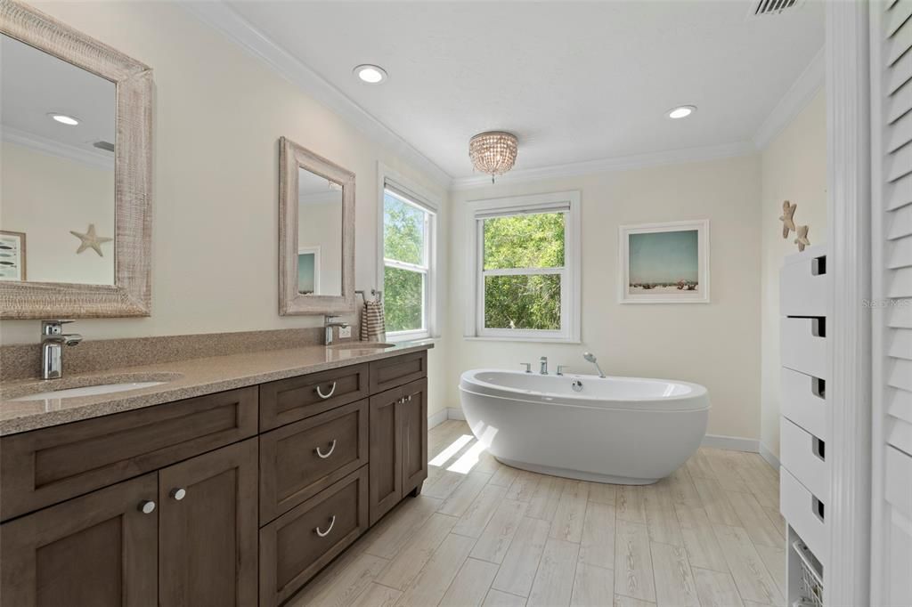 The custom updated spa-like primary bathroom features exquisite natural light, a large walk-in shower, a luxurious soaking tub, quartz counters &  tile plank floors.