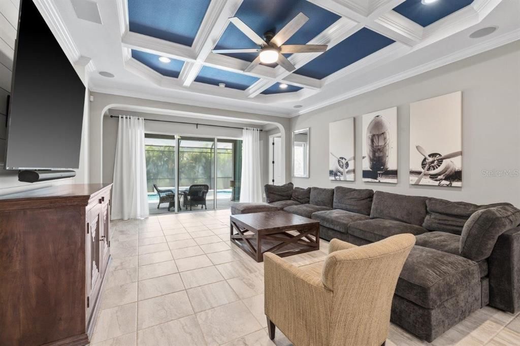 Living Room featuring a coffered ceiling, crown molding, shiplap, and a large 3 panel sliding glass door out to the screened-in lanai and heated pool.