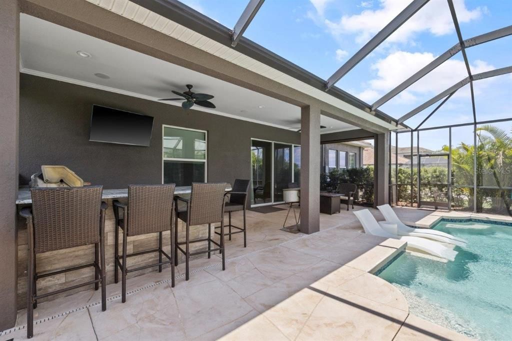 Extended screened-in lanai featuring a heated pool with a sun shelf, and full outdoor kitchen.