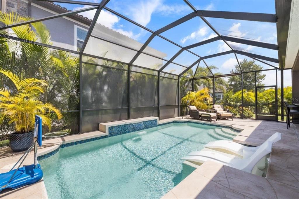 Extended screened-in lanai featuring a heated pool with a sun shelf, and full outdoor kitchen.