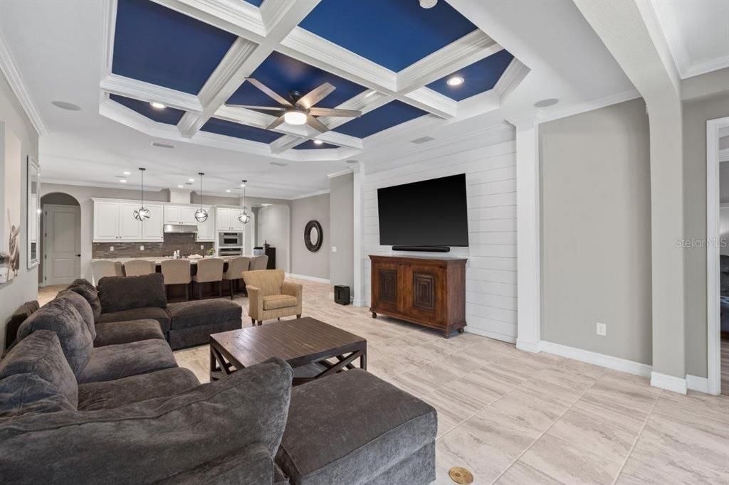 Living Room featuring a coffered ceiling, crown molding, shiplap, and a large 3 panel sliding glass door out to the screened-in lanai and heated pool.