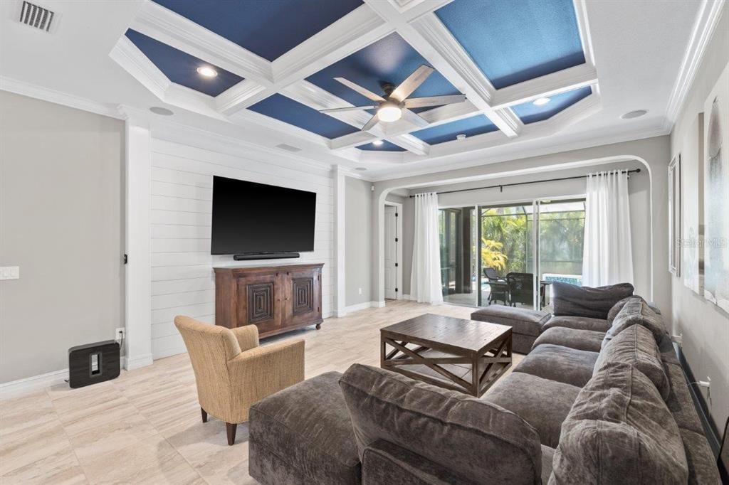 Living Room featuring a coffered ceiling, crown molding, shiplap, and a large 3 panel sliding glass door out to the screened-in lanai and heated pool.