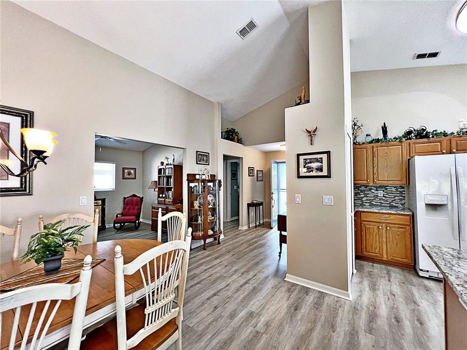 View from living room of dining room, den, entry, and kitchen. With vaulted ceilings, laminate flooring throughout, and freshly painted.