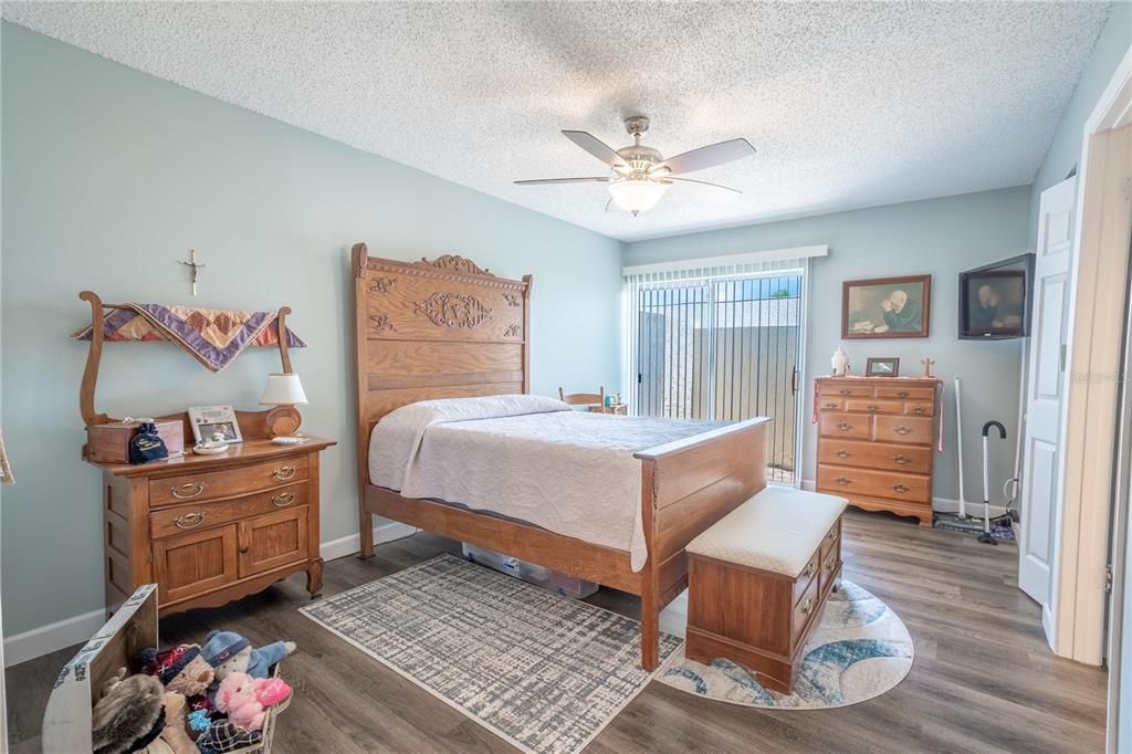 Primary bedroom has sliding glass doors  that open to a private patio. It also features two walk-in closets, vinyl plank flooring and a ceiling fan with light kit.