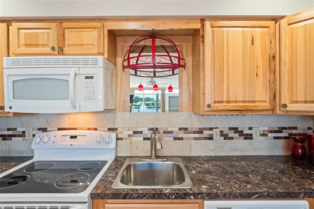 Kitchen has a flat top stove, tile back splash and stainless-steel sink.