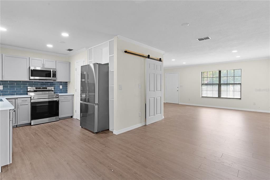 Kitchen and dining area with living room and front door just past the barn door which is the laundry room