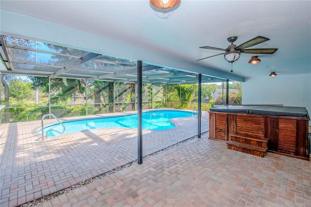 Screened in Pool with Pavers and View of Hot Tub and Lush Landscaping