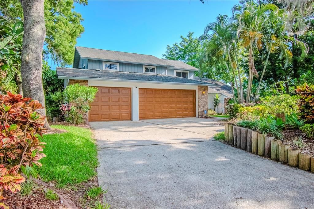 Front of Property showing Large Driveway, 3-Car Garage with Newer Garage Doors (2017) and Walkway to Entrance and Lush Mature Landscaping