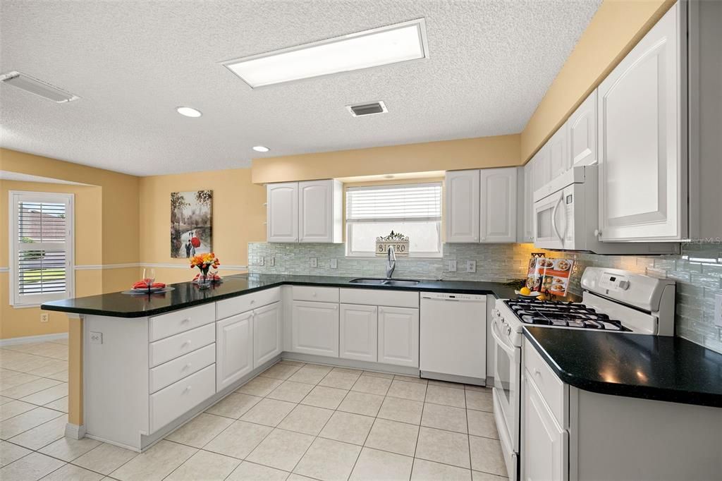 The inviting, eat-in kitchen features white cabinets, Double pantry with pull out shelves, glass tiled backsplash, and a gas stove, making it a perfect space for culinary enthusiasts.