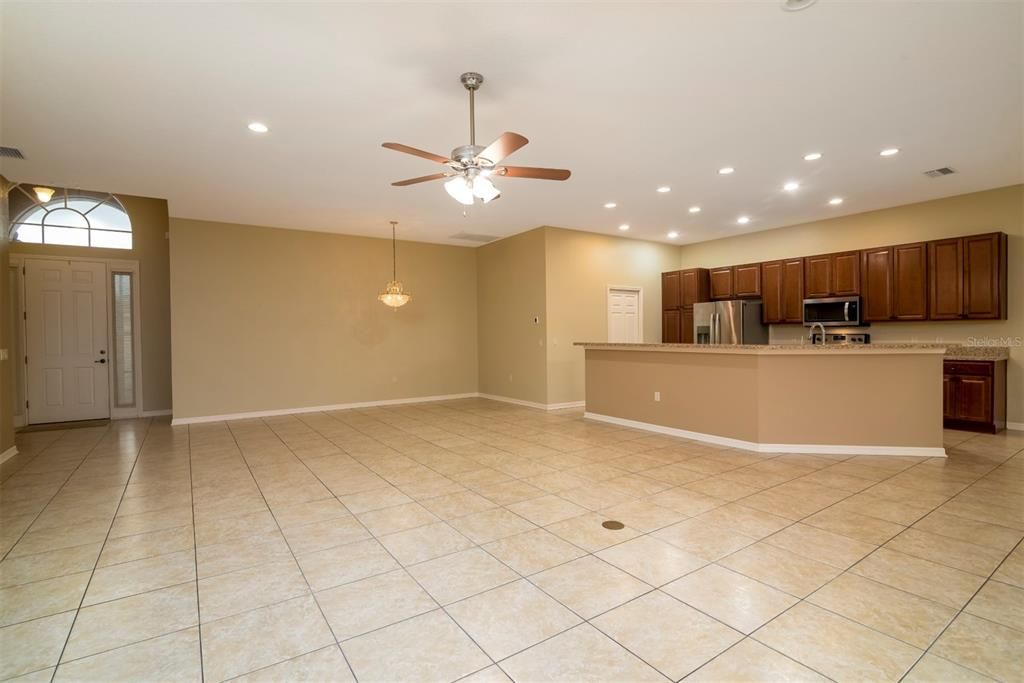 The living room has a ceiling fan with light and a floor outlet. The dining room area is in the background.