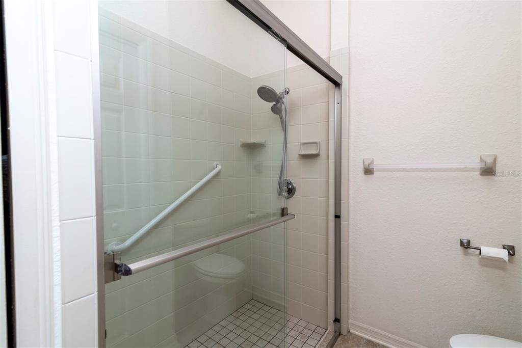 The master bath has a stall shower with glass shower door and grab bar. The elongated handicapped height dual flush toilet is on the right.