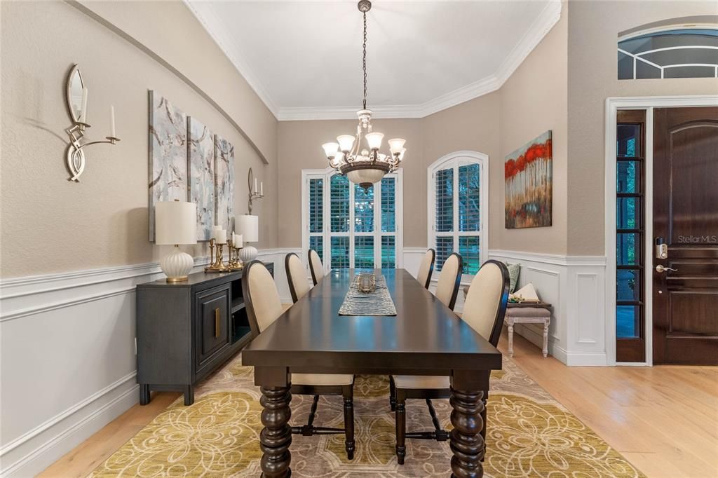 The elegant dining room, adorned with crown molding and chandelier, is adjacent to the grand entryway with a solid wood door.
