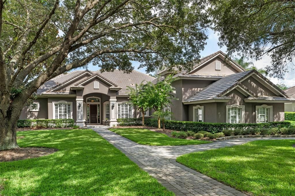 This custom-built home is framed by mature trees and lush landscaping, offering a warm and inviting first impression.
