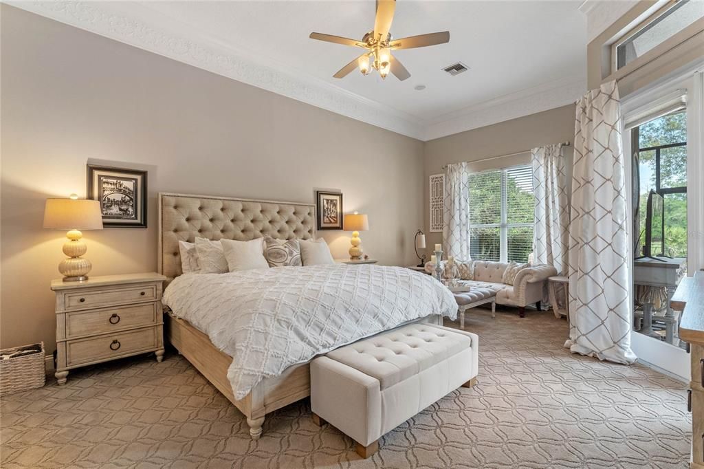 The spacious primary bedroom features elegant crown molding, plush carpeting, and private access to the outdoor living area, creating a luxurious retreat.