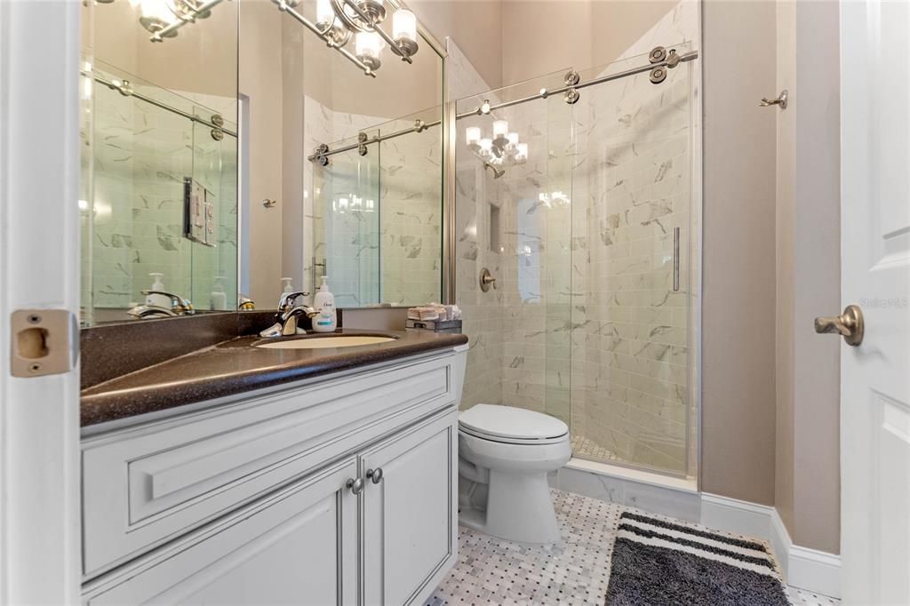 The stylish pool bath offers convenience and elegance with its modern vanity, glass-enclosed shower, and chic finishes, perfect for guests and poolside access.