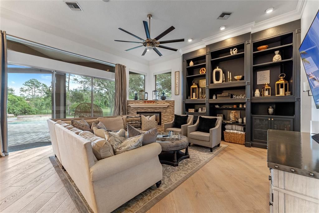 The spacious family room offers custom built-in shelving, a cozy fireplace, and expansive views of the pool and golf course.