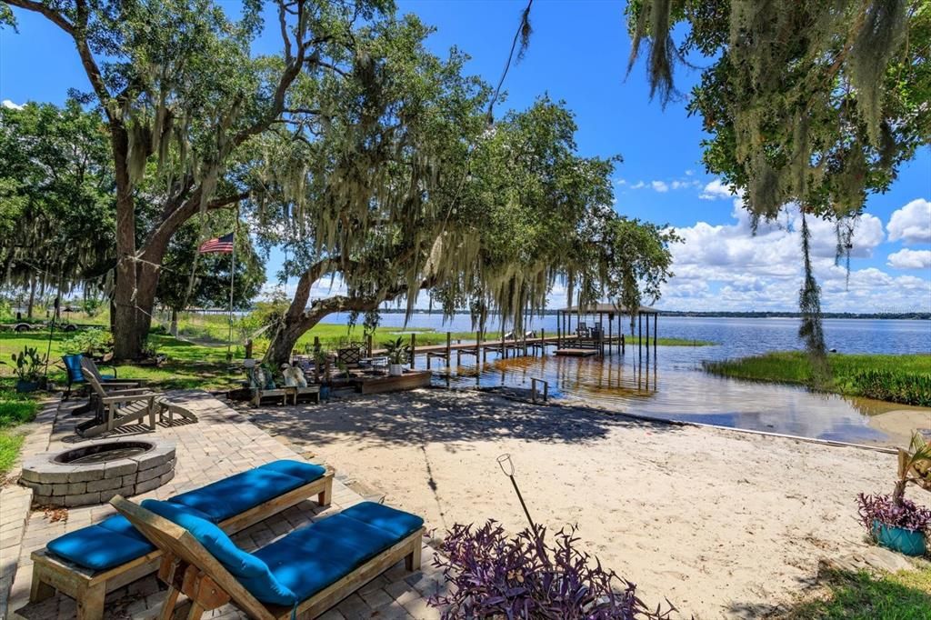 Brick pavered area down by the lake with fire pit and sandy beach.