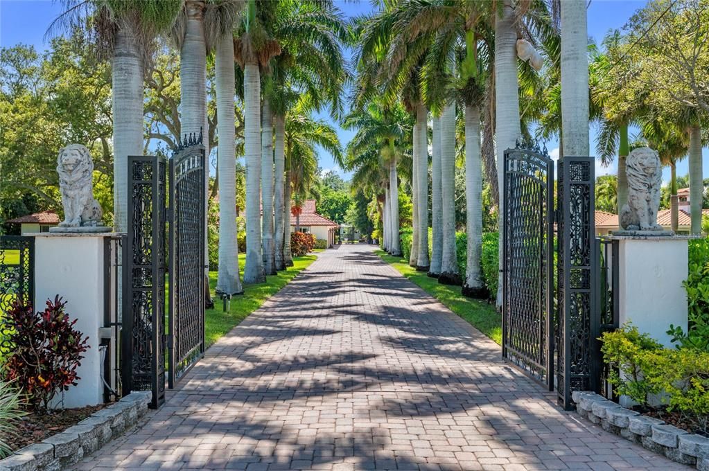 This picturesque driveway is lined with majestic palm trees, creating a grand and serene approach to the home. The wrought-iron gates, adorned with intricate designs and flanked by regal lion statues, enhance the estate's sense of security and sophistication. The brick-paved path leads through lush greenery and meticulously maintained landscaping, setting the tone for the luxurious living experience that awaits.