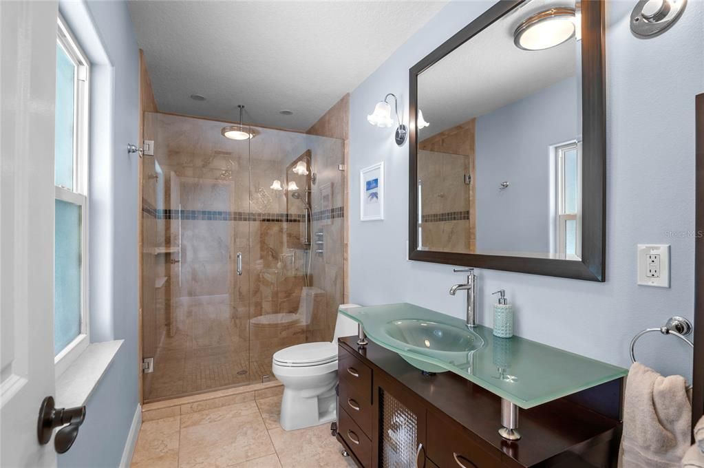 In-law suite bathroom.. The contemporary bathroom features a sleek glass vessel sink, a modern vanity, and a spacious walk-in shower with elegant tile work and a glass enclosure.