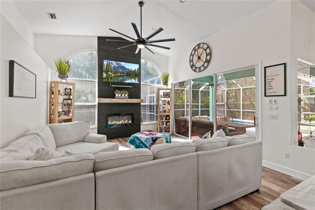 Spacious family room with feature wall that includes electric fireplace, custom mantle and large sliding doors extending to spacious covered and enclosed pool and patio.