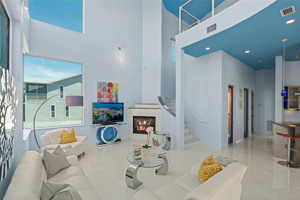 The 2-story living room boasts a soaring ceiling, impressive windows, screened terrace access, and electric fireplace that creates a relaxing ambiance.