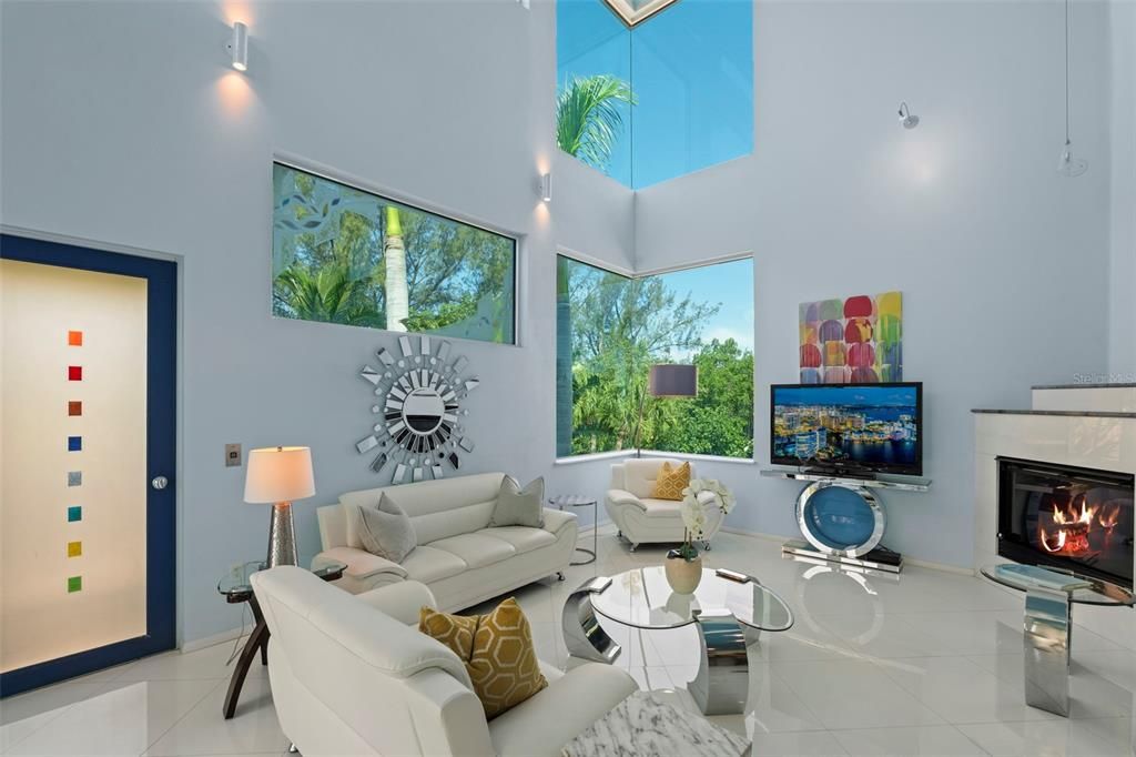 The 2-story living room boasts a soaring ceiling, impressive windows, screened terrace access, and electric fireplace that creates a relaxing ambiance.