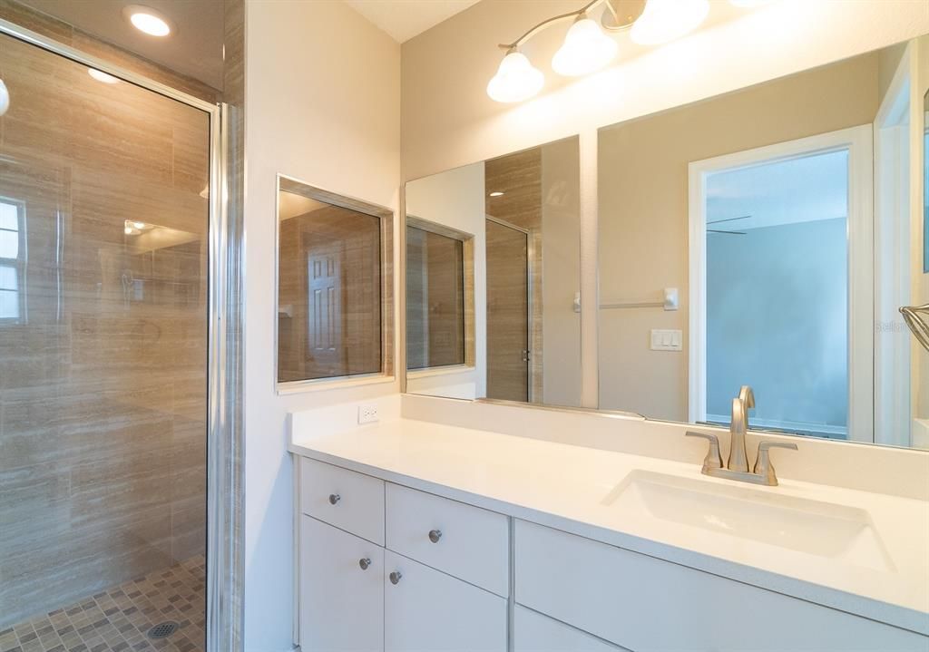 remodeled primaty bath with quartz countertop, single sink vanity area and enclosed shower.