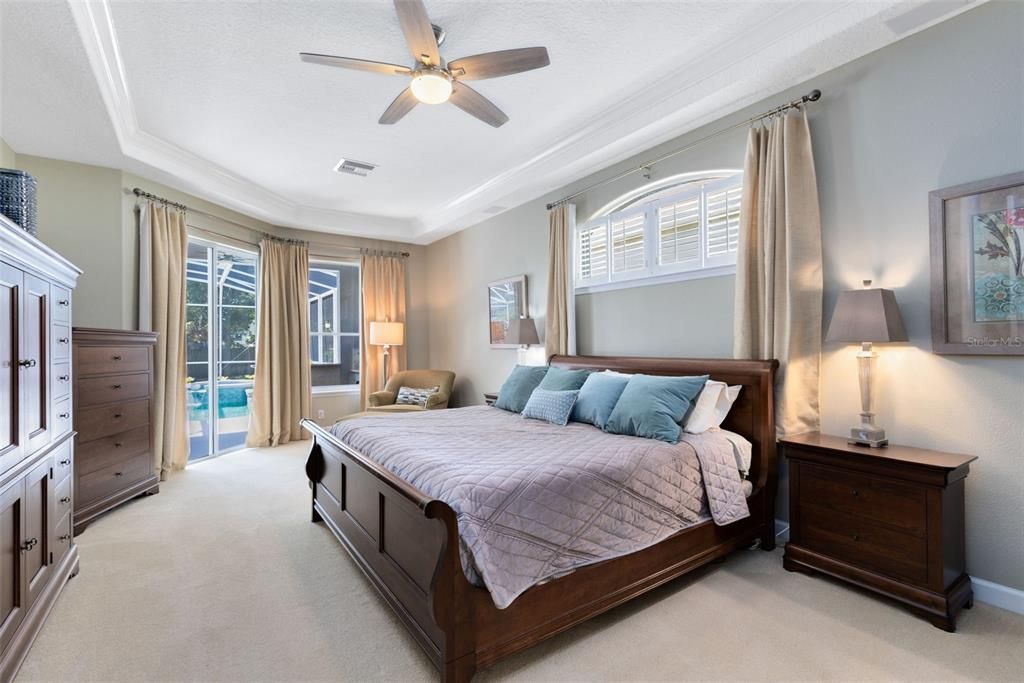 Primary bedroom with tray ceiling and slider out to the pool