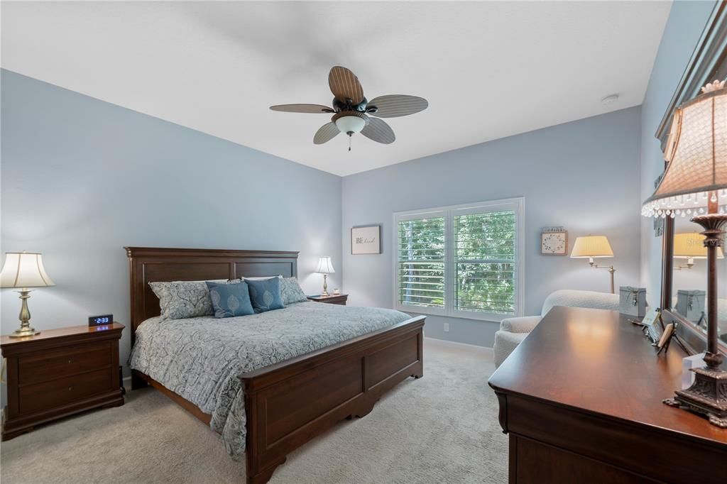 Primary bedroom features custom plantation shutters and peaceful wooded views