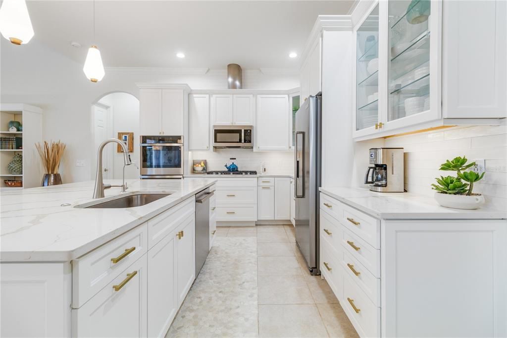 Kitchen is a dream for those who love to cook with quartz countertops, tile backsplash, upper and under cabinet lighting, ample cabinet spaces, which are beautifully ornamented with a touch of gold handles.