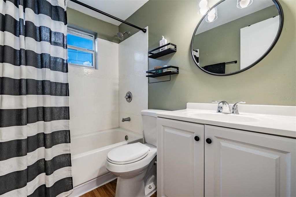 Updated bathroom is modern and fresh with white vanity and shower surround.