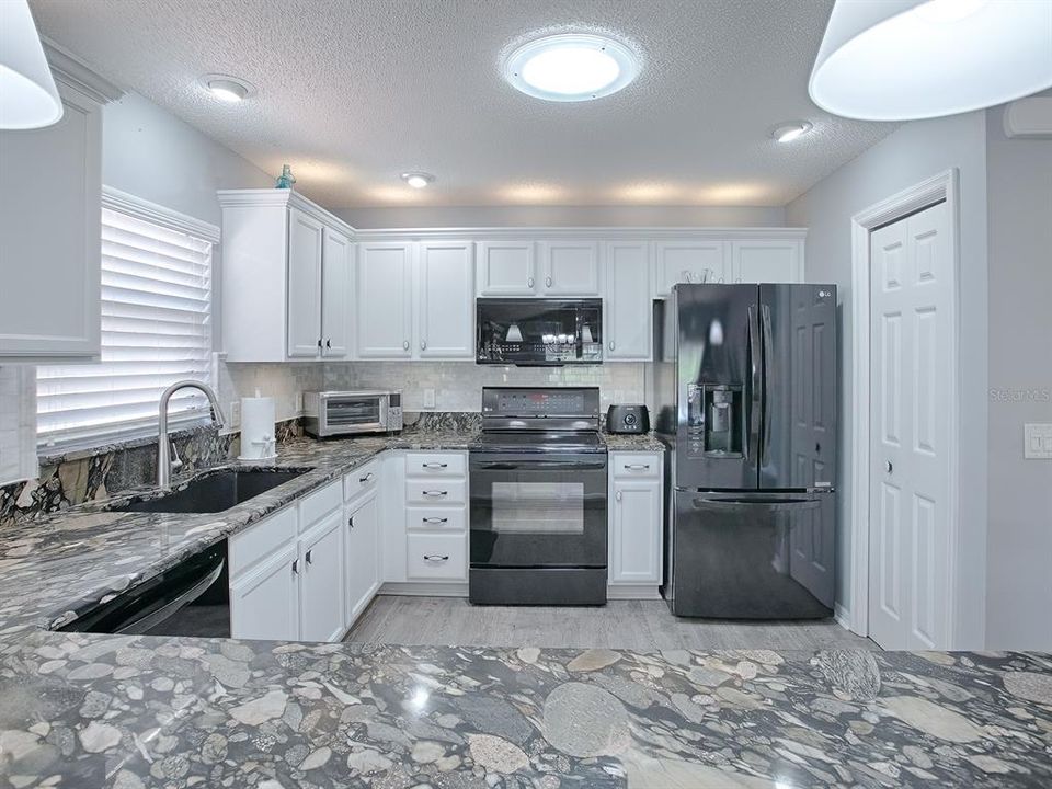 STRIKING GRANITE COUNTER TOPS WITH SUBWAY TILE BACKSPLASH, NEW SINK, FAUCET, FIXTURES AND A SOLAR TUBE FOR NATURAL LIGHTING.