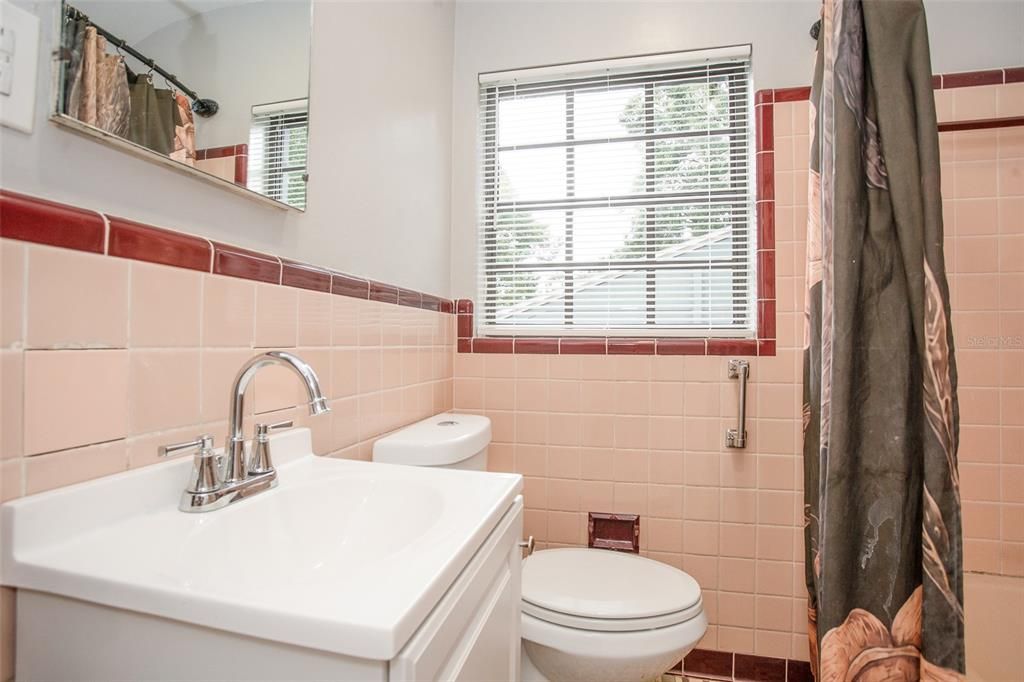 The main bathroom features a mirrored vanity with storage, vintage ceramic tile, and a tub with shower.