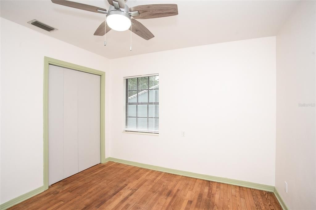 The bedroom 2 features oak wood floors, a ceiling fan and a built-in closet.