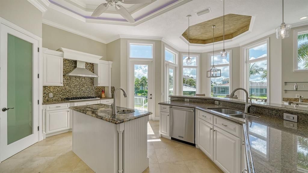 Kitchen has tray ceiling with custom lighting, island with center sink, beverage cooler, and walk in pantry