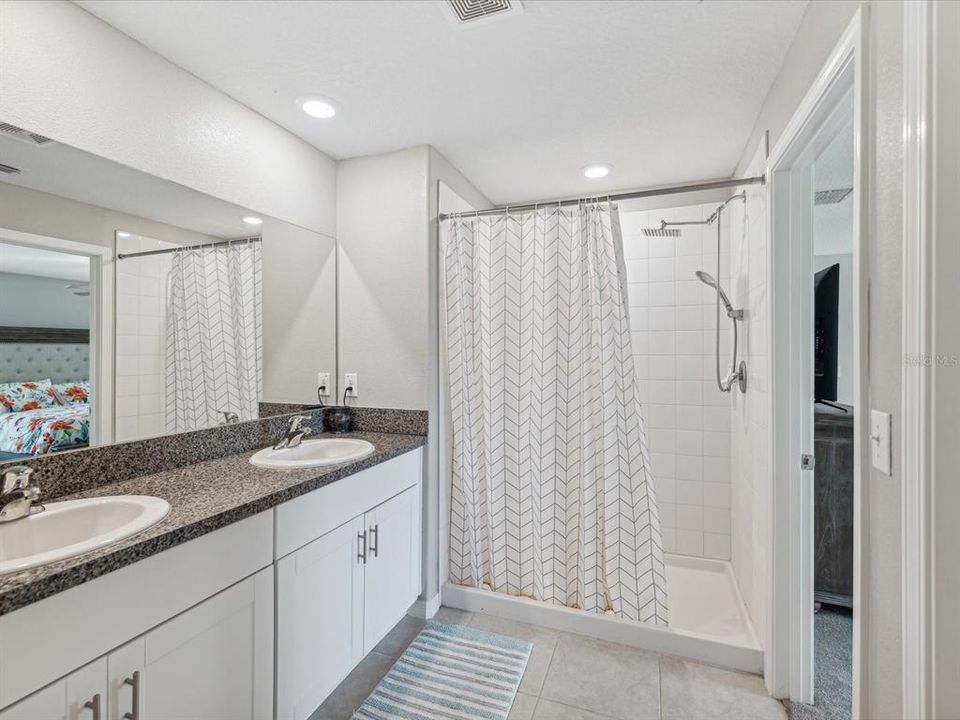 En-suite primary bathroom with dual sink vanity, wood base cabinets, separate toilet closet, and a large shower