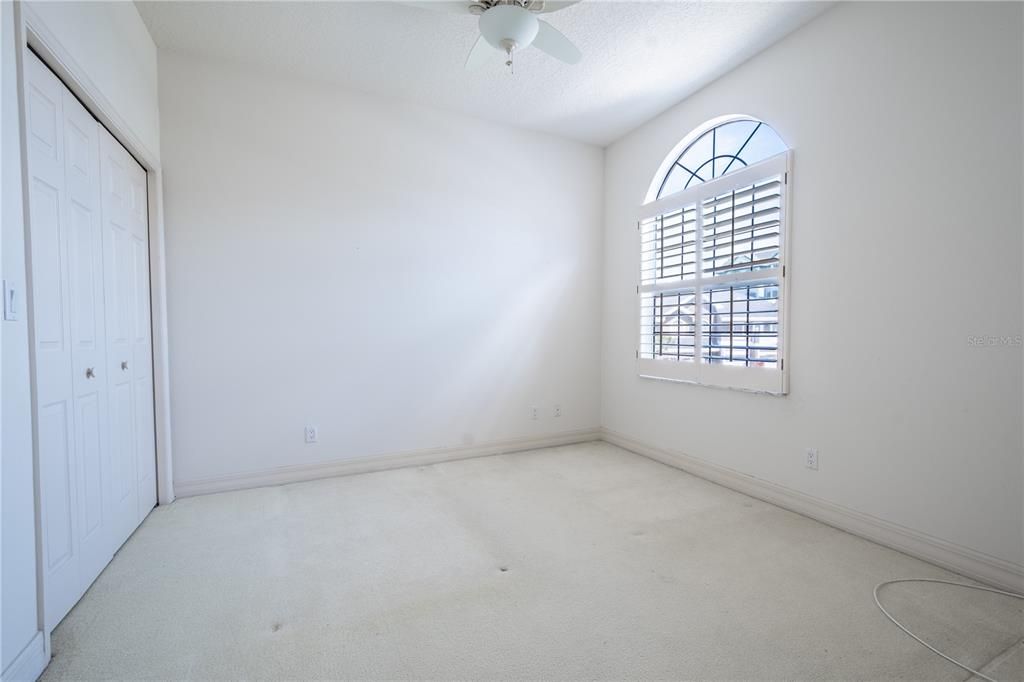 Bedroom 2 features a built-in closet, a ceiling fan with light kit, plantation shutters, and neutral tone walls and carpet.