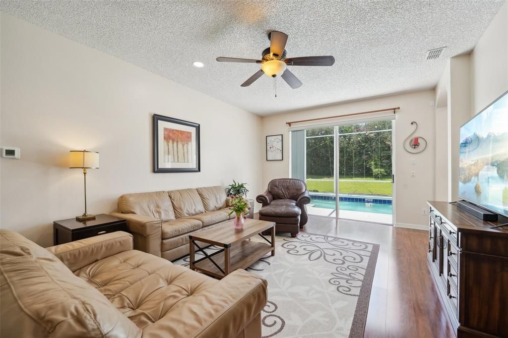 THE MAIN FAMILY ROOM that OVERLOOKS THE BEAUTIFUL POOL through OVERSIZED SLIDERS & is also complimented by NEWER LAMINATE FLOORING, HIGH CEILINGS, FRESH PAINT & NEW FIXTURES.