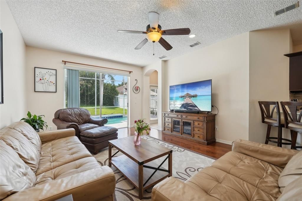 THE MAIN FAMILY ROOM that OVERLOOKS THE BEAUTIFUL POOL through OVERSIZED SLIDERS & is also complimented by NEWER LAMINATE FLOORING, HIGH CEILINGS, FRESH PAINT & NEW FIXTURES.