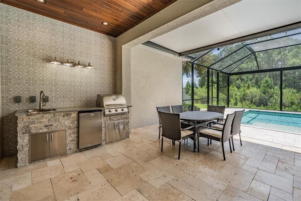 Outdoor kitchen with grill, sink, refrigerator and tiled wall