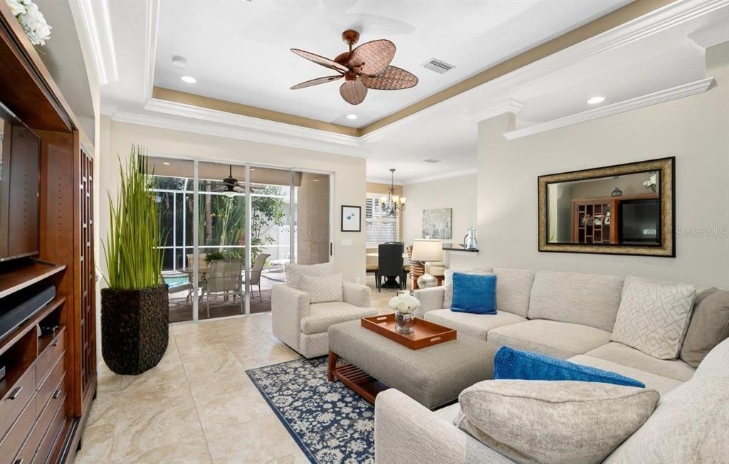 Spacious great room featuring 16" tile, 10' tray ceilings, custom built-ins, and a 4 panel sliding glass door that leads out to the screened-in lanai and heated pool.