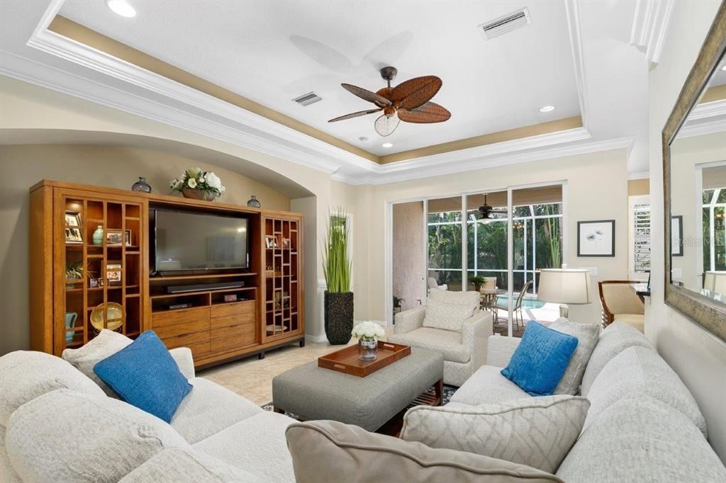 Spacious great room featuring 16" tile, 10' tray ceilings, custom built-ins, and a 4 panel sliding glass door that leads out to the screened-in lanai and heated pool.