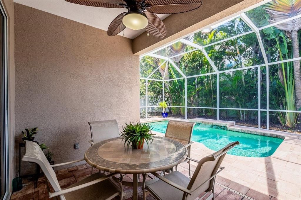 Screened-in Covered lanai featuring a solar heated pool, a sitting area, and an extended paver walkway/storage area.