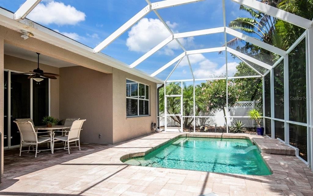 Screened-in Covered lanai featuring a solar heated pool, a sitting area, and an extended paver walkway/storage area.