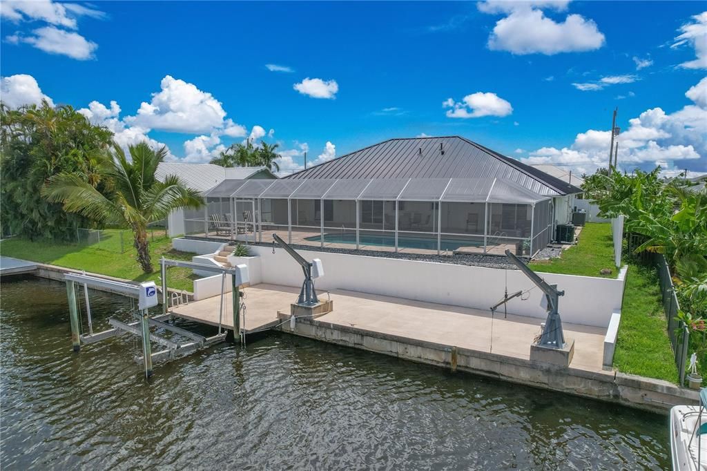 View of dock with a lawn, glass enclosure, a water view, and a patio