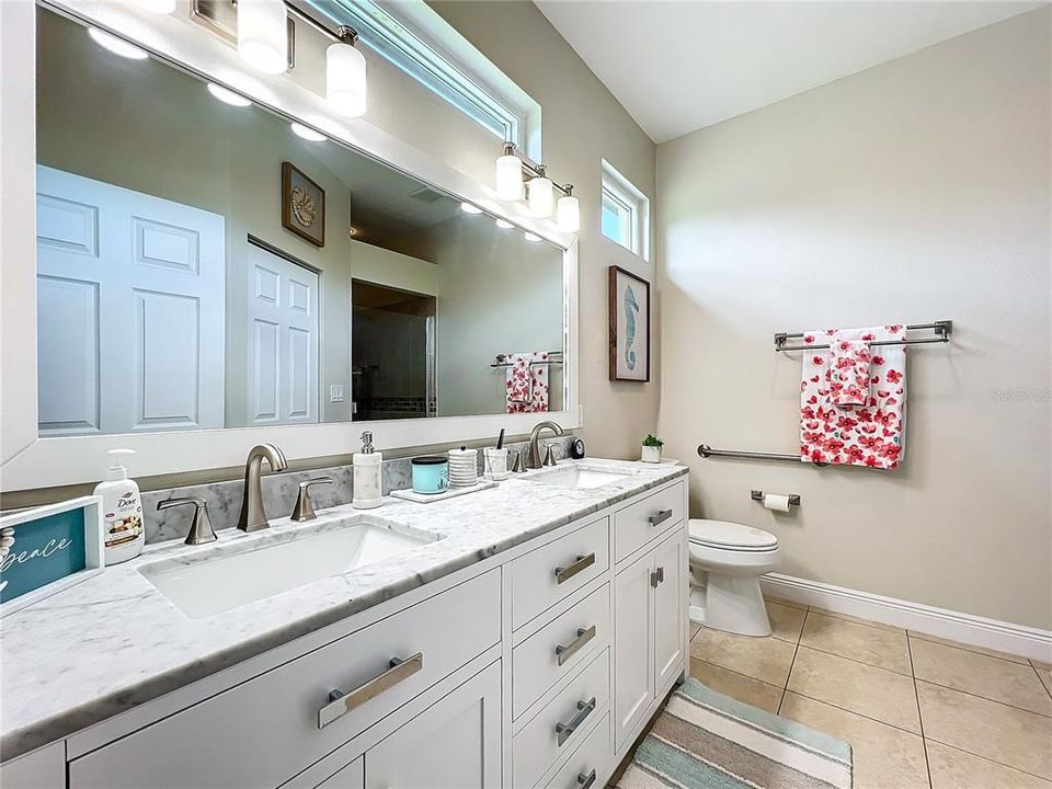 Primary ensuite bathroom with dual sinks, white cabinets, and clerestory windows for additional lighting .