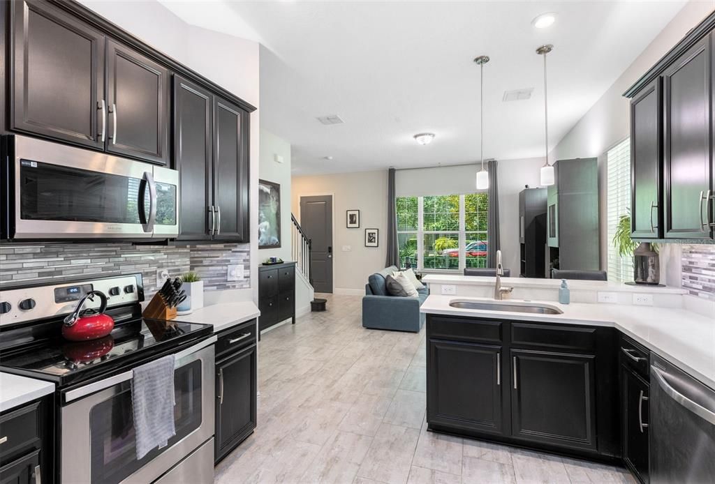 featuring undercabinet lighting, quartz countertops with a breakfast bar, stainless steel appliances, a stylish tile backsplash, and a convenient walk-in pantry.